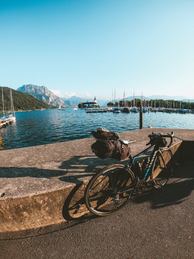Anja's Rennrad mit Bikepacking-Ausstattung am Ufer des Traunsees mit Blick auf Schloss Ort und den Traunstein.